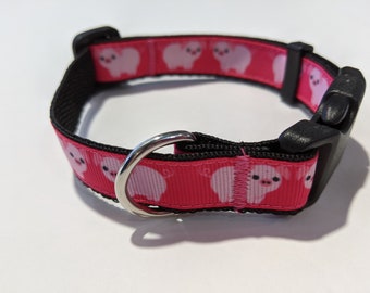 May include: A pink dog collar with a black buckle and a silver ring. The collar is decorated with a repeating pattern of pink pigs.