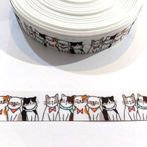 May include: White satin ribbon with a repeating pattern of colorful cartoon cats. The cats are all different colors and have different expressions.