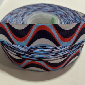 May include: A roll of blue, red, and white wavy patterned ribbon. The ribbon is on a spool and is ready to be used for crafting or decorating.