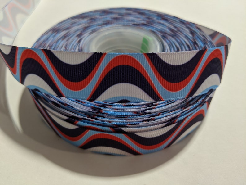 May include: A roll of blue, red, and white wavy patterned ribbon. The ribbon is on a spool and is ready to be used for crafting or decorating.