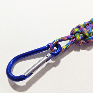 May include: A blue metal carabiner clip attached to a multi-colored paracord lanyard. The paracord is woven in a complex pattern with pink, yellow, and blue.