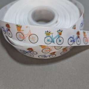 May include: White ribbon with a repeating pattern of bicycles with baskets of flowers. The bicycles are in shades of blue, green, and pink.