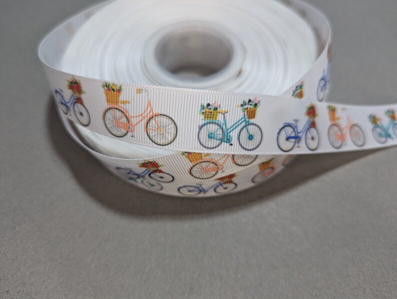 May include: White ribbon with a repeating pattern of bicycles with baskets of flowers. The bicycles are in shades of blue, green, and pink.
