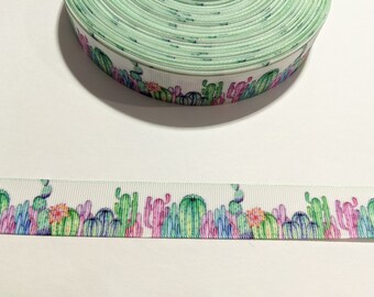 May include: White ribbon with a green, pink, and blue cactus print. The ribbon is rolled up and the print is visible on the side of the roll.