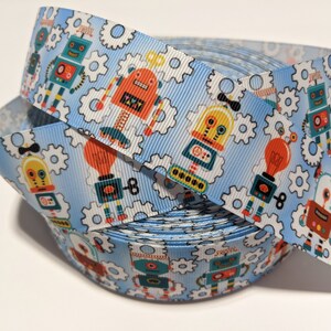 May include: A roll of blue ribbon with a repeating pattern of colourful robots and gears. The robots are in various poses and have different facial expressions.