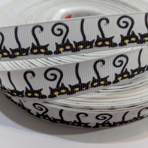 May include: White ribbon with a repeating pattern of black cats with curled tails and yellow eyes.