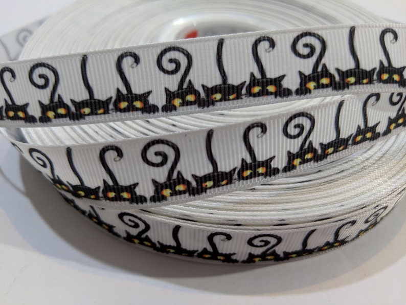 May include: White ribbon with a repeating pattern of black cats with curled tails and yellow eyes.