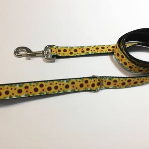 May include: A yellow and green dog leash with a sunflower pattern. The leash has a silver clip and a silver ring.
