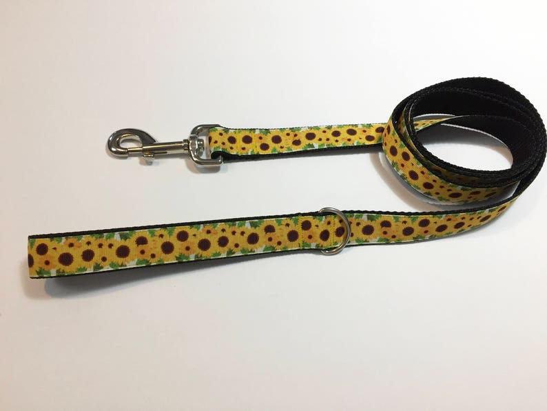 May include: A yellow and green dog leash with a sunflower pattern. The leash has a silver clip and a silver ring.