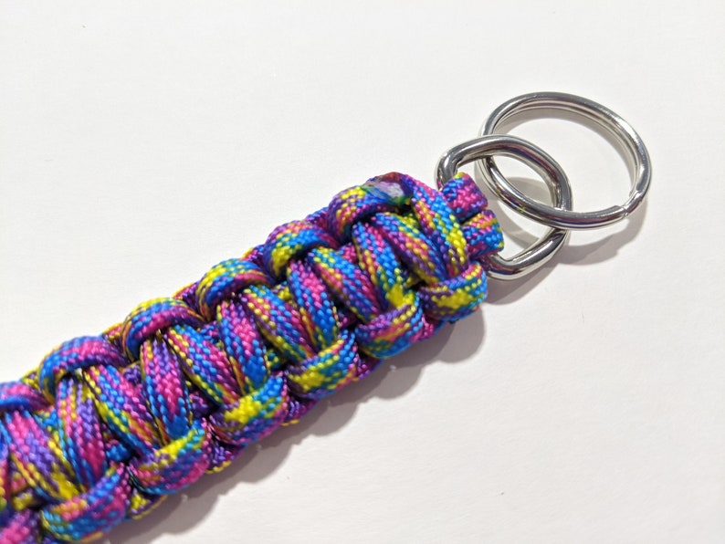 May include: A colorful paracord keychain with a silver key ring. The paracord is woven in a pattern of pink, blue, yellow, and green.