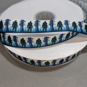 May include: A roll of white satin ribbon with a repeating pattern of black Bigfoot silhouettes walking through a blue and white forest.