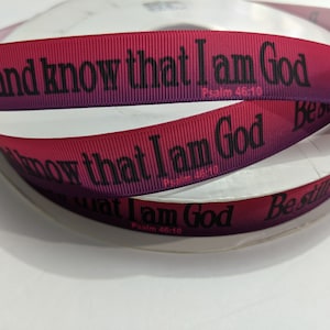 May include: Spool of red and purple ombre ribbon with the text "Be still and know that I am God, Psalm 46:10" printed in black. The ribbon is likely used for crafting or gift wrapping.
