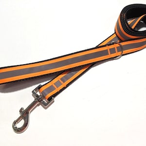 Peut inclure: Une laisse de chien noire et orange avec des bandes réfléchissantes et un mousqueton argenté.