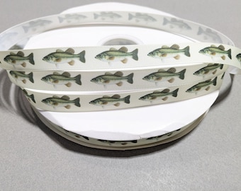 May include: A spool of off-white grosgrain ribbon featuring a repeating pattern of green and brown largemouth bass fish. The ribbon is wound around a white circular plastic core, displaying multiple layers of the fish-themed fabric trim.