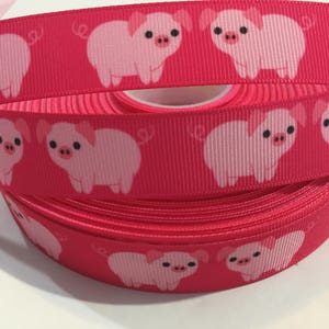 May include: Pink and red ribbon with a repeating pattern of pink pig illustrations. The pigs have curly tails and are facing to the right.