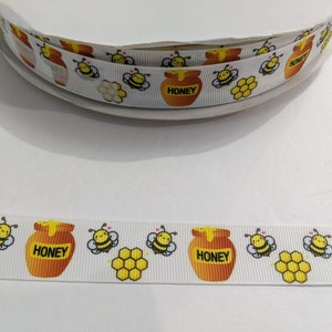 Peut inclure: Ruban blanc avec un motif répété de pots de miel, de nids d'abeilles et d'abeilles de dessin animé. Les pots sont étiquetés "Honey".
