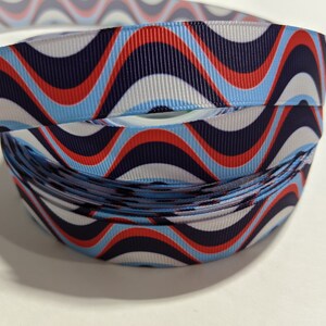 May include: A roll of blue, white, and red wavy patterned ribbon. The ribbon has a repeating pattern of waves in red, white, and blue.