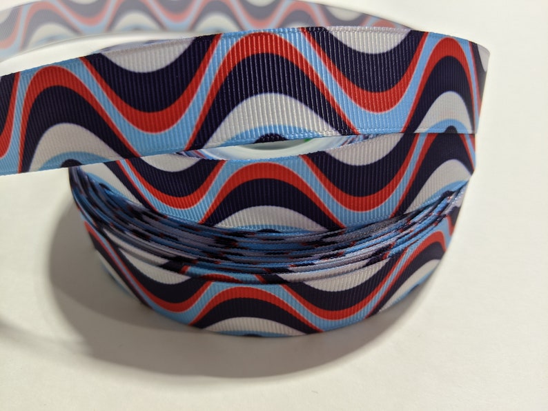 May include: A roll of blue, white, and red wavy patterned ribbon. The ribbon has a repeating pattern of waves in red, white, and blue.
