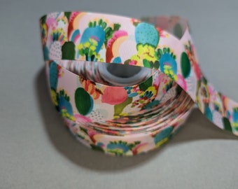 May include: A roll of pink ribbon with a colorful cactus print. The ribbon is rolled up and has a white spool in the center.
