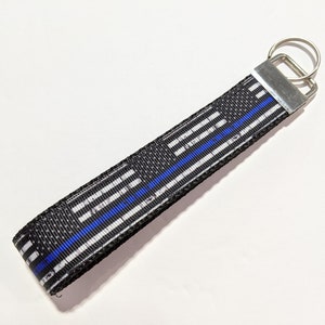 Può includere: Portachiavi con motivo bianco e nero con una striscia blu e un anello portachiavi argentato.