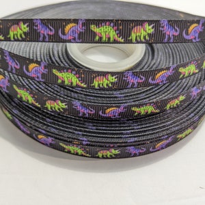 May include: Black ribbon with a repeating pattern of colorful dinosaurs. The ribbon is wound around a spool.