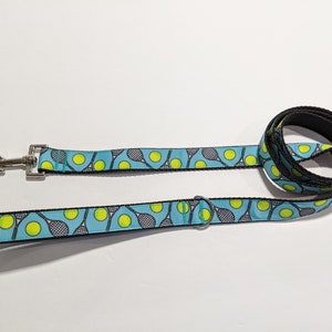 May include: A blue and black dog leash with a tennis racket and ball pattern.