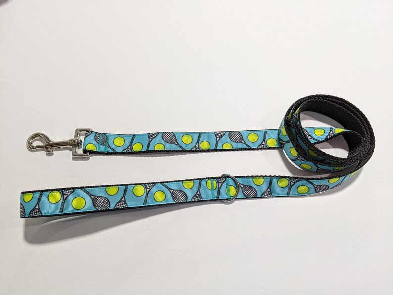 May include: A blue and black dog leash with a tennis racket and ball pattern.