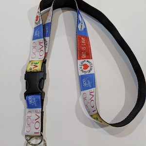May include: A lanyard with the words "GOD IS LOVE" printed on a colorful ribbon. The ribbon has a blue, red, and yellow background. The lanyard has a black clasp and two silver key rings.