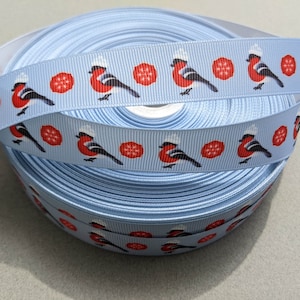 May include: A roll of light blue ribbon with a repeating pattern of red robins wearing white hats and red snowflakes.