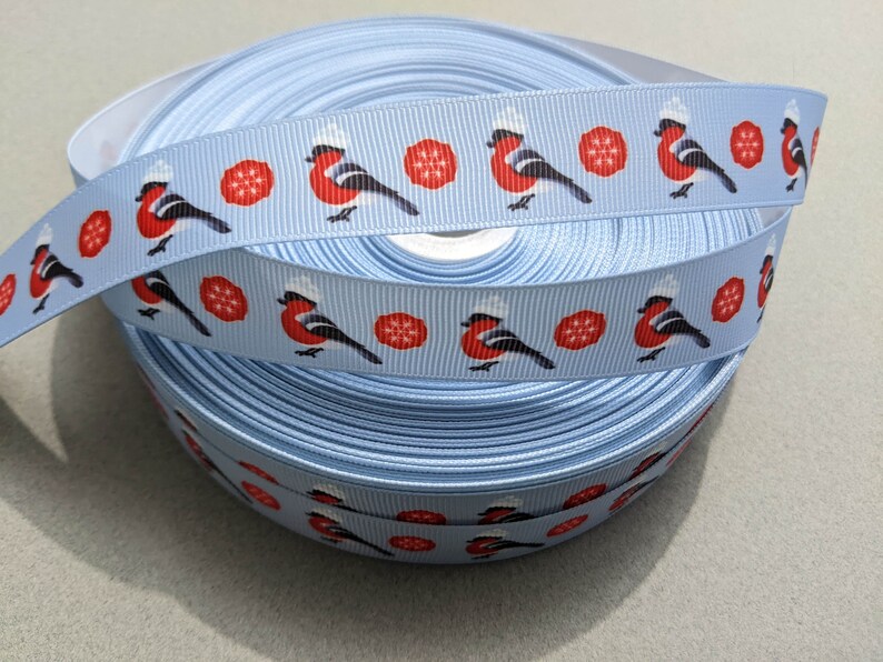 May include: A roll of light blue ribbon with a repeating pattern of red robins wearing white hats and red snowflakes.