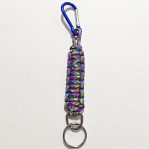 May include: A colorful paracord keychain with a blue carabiner and a silver key ring. The paracord is woven in a pattern of pink, yellow, and blue.