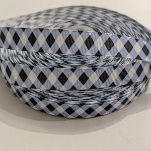 May include: A spool of grosgrain ribbon featuring a repeating argyle pattern in light blue, black, and white. The ribbon is wound into a tight circular coil, displaying the diamond-shaped geometric design across the entire visible surface area.
