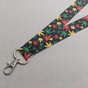 May include: A black lanyard with a green, yellow, and red leaf pattern. The lanyard has a silver swivel clip.