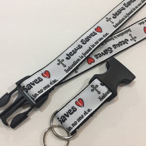 May include: White lanyard with black text that reads "Jesus Saves" and "Salvation is found in no one else." The lanyard has a black plastic clasp and a metal keyring.