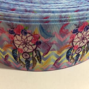 Pu&ograve; includere: Primo piano di un nastro blu e rosa con un motivo di acchiappasogni. Il nastro ha un motivo a chevron e presenta fiori rosa e piume.