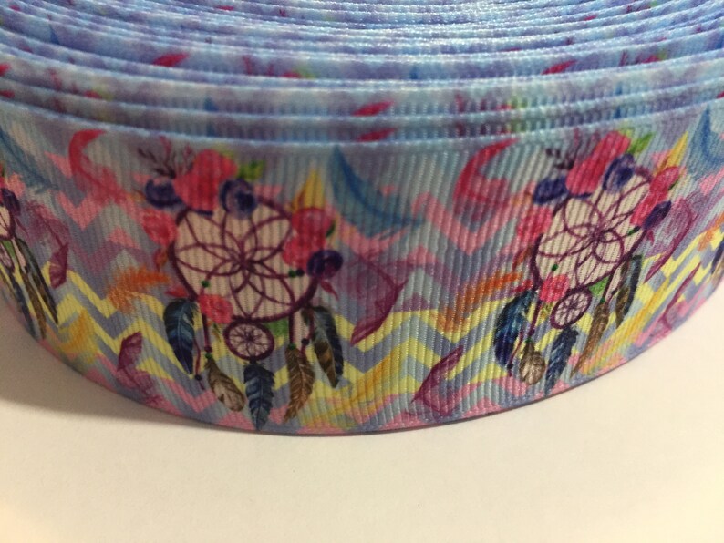 Pu&ograve; includere: Primo piano di un nastro blu e rosa con un motivo di acchiappasogni. Il nastro ha un motivo a chevron e presenta fiori rosa e piume.