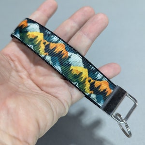 May include: A black and yellow mountain scene printed on a key chain with a silver metal ring.