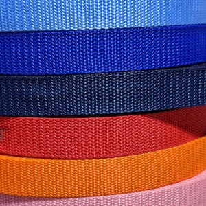 May include: A stack of colorful nylon webbing in various shades, including black, green, gray, blue, red, orange, pink, brown, and purple. The webbing has a tightly woven texture, suitable for straps or belts.