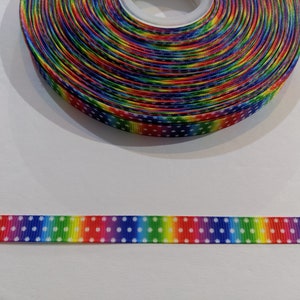 Peut inclure: Ruban arc-en-ciel avec des pois blancs. Le ruban est enroulé et une petite section est déroulée pour montrer le motif.