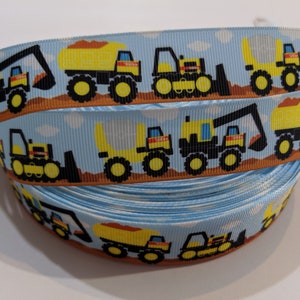 May include: A blue and brown ribbon with a repeating pattern of yellow construction vehicles. The vehicles include a dump truck, an excavator, and a bulldozer.