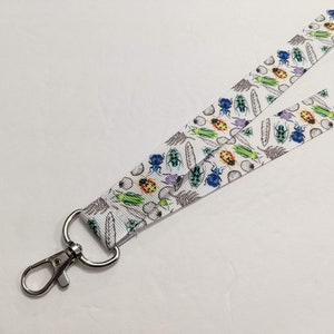 May include: White lanyard with a colorful bug pattern and a silver swivel clip.