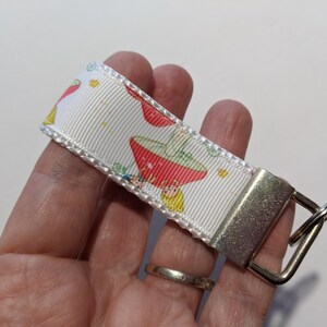 May include: White key chain with a silver key ring. The key chain has a white ribbon with a red and green mushroom pattern.