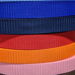 May include: A stack of 13 different colored webbing straps. The straps are all the same width and are arranged in a stack from top to bottom. The colors are black, gray, light blue, blue, navy blue, red, orange, pink, brown, purple, royal blue, and yellow.