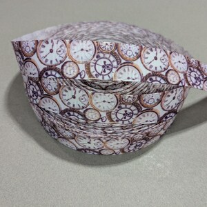 May include: A roll of white satin ribbon with a repeating pattern of vintage-style clocks in shades of brown and gold.