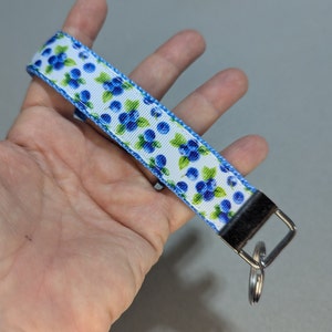 May include: A white and blue patterned key chain with a silver key ring. The pattern features blueberries and green leaves.