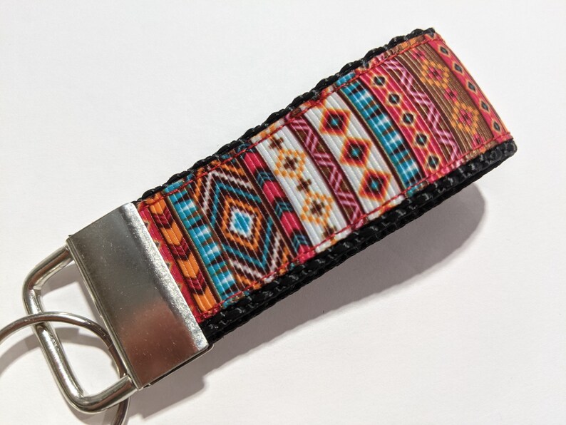 May include: A colorful key chain with a geometric pattern in shades of orange, red, blue, brown, and white. The key chain has a silver metal key ring and a black strap.