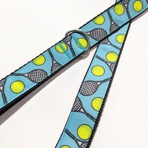 May include: A blue dog leash with a tennis racket and ball pattern. The leash has a silver metal ring.