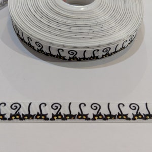 May include: White ribbon with a black cat design. The ribbon is rolled up and the design is visible on the edge of the roll.