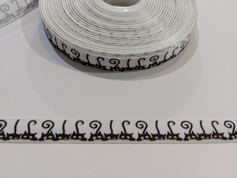 May include: White ribbon with a black cat design. The ribbon is rolled up and the design is visible on the edge of the roll.