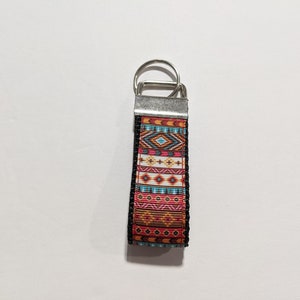 May include: A colorful key chain with a geometric pattern in shades of orange, red, blue, and white. The key chain has a silver metal ring and a black border.